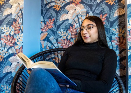 A young woman enjoys reading a book, seated in a modern chair against a colorful floral-patterned
