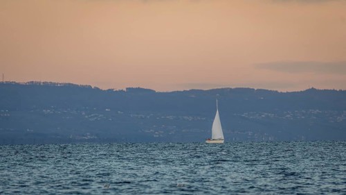 A serene scene of a sailboat gracefully moving across a calm lake in Geneva, set against a backdrop