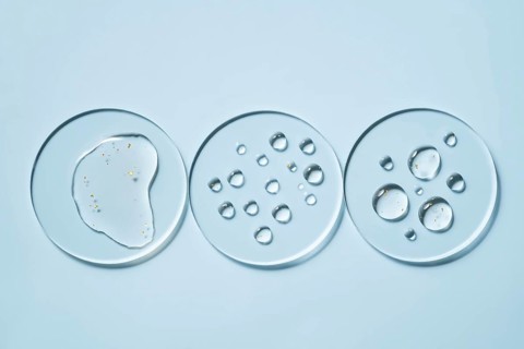 Three transparent petri dishes with water droplets placed on a light blue surface The circular