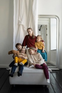 Five children, dressed in vibrant outfits, sit and play together in a cozy room with a large mirror