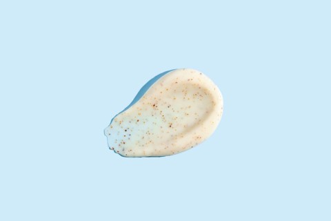 A dab of exfoliating cream with visible scrub particles smeared on a pastel blue background