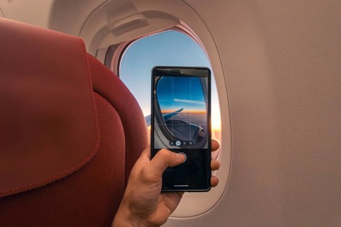 Cropped unrecognizable person captures a sunset over the ocean using a smartphone, viewed through