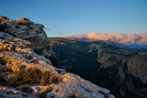 A stunning landscape of rocky cliffs and forested valleys illuminated by the warm light of sunset,