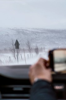 A hand captures a snowy landscape from inside a vehicle, showcasing the tranquil and harsh beauty