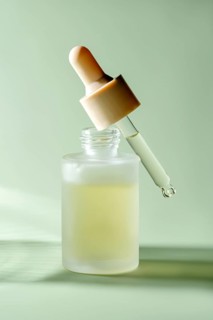 A translucent serum dropper bottle with a single drop hanging from the pipette, showcased against a