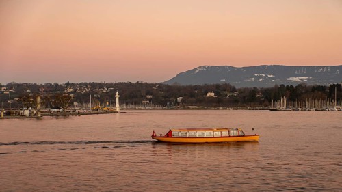 A vibrant yellow boat glides across the serene waters of Lake Geneva during a stunning sunset, with