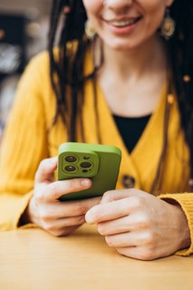 A woman in a mustard yellow sweater holds a smartphone with a green case, smiling The cozy setting