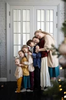 A loving family of six embraces warmly in front of a white-paneled doorway Their cozy clothing and