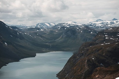 A sweeping view of a tranquil lake nestled in a dramatic mountain valley in Norway Snow-dusted