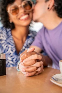 A cheerful multiethnic LGBTQ+ couple seated at a table, holding hands and sharing a tender moment,