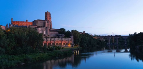 A stunning view of historic Berbie Palace en Albi, with serene waters reflecting the evening sky