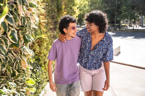A happy, multiethnic LGBTQ+ couple walking side by side, smiling under the sunlight. Their warm