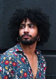 Portrait of a stylish man with curly hair wearing hoop earrings and a vibrant floral shirt. The