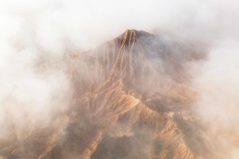 A breathtaking mountain peak emerges through a dense layer of clouds, showcasing its rugged terrain