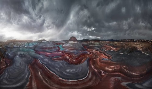 A mesmerizing landscape of colorful, striped geological formations under a dramatic, cloudy sky.
