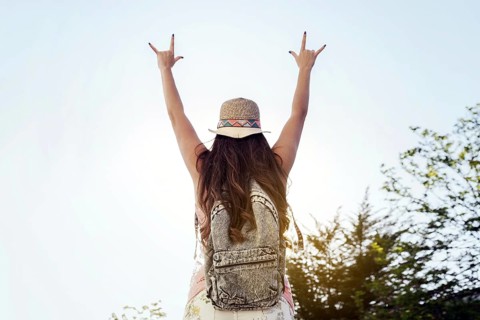 A woman wearing a hat and backpack raises her arms in a joyful sign, celebrating freedom and nature
