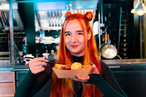 A woman with red hair delights in Asian street food at a lively market She holds chopsticks and a