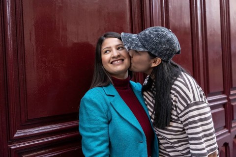 A loving Latin lesbian couple shares a sweet moment by a burgundy wall. One partner playfully