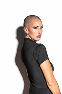 Portrait of a middle-aged woman with a shaved head in a black top, exuding confidence. She is