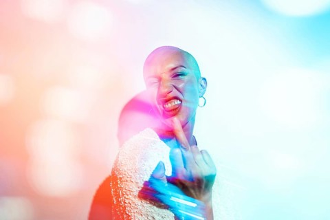 A bold woman expressing defiance with her middle finger towards camera, surrounded by vibrant,