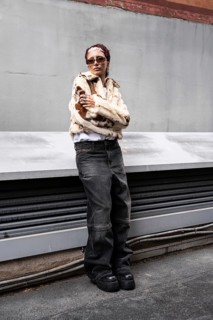 A woman confidently poses in a trendy fur jacket and sunglasses, embodying urban street style.