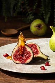 Close up of ripe figs sliced open, drizzled with golden honey. Pomegranate seeds scattered on a