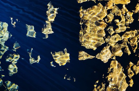 Sunlight reflecting on water, illuminating rocks below. The combination of light and texture