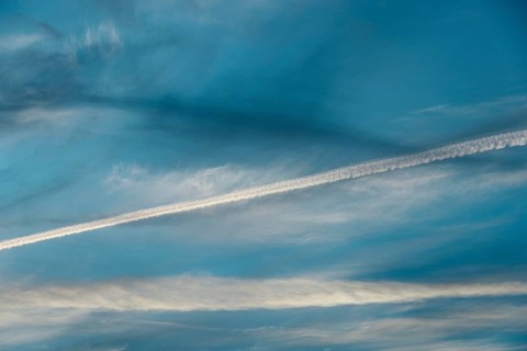 Airplane contrail across a clear blue sky. The white streak contrasts beautifully with the soft