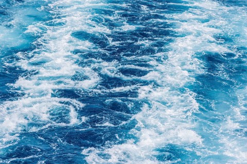 Turbulent sea waves with foam and ripples in deep blue water. The movement captures the raw power