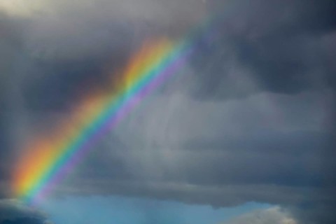 A stunning photograph capturing a vivid rainbow arching over a dark, stormy sky, showcasing the