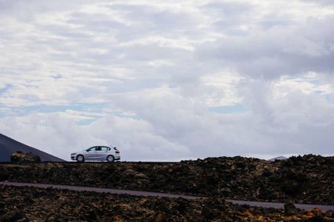 Car on a lonely road surrounded by a volcanic landscape. The rocky formations emphasize the