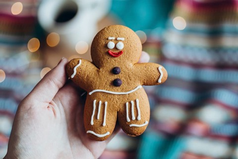Hand holding a cheerfully decorated gingerbread man cookie, featuring icing details, with a