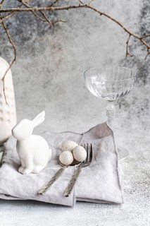 An elegant Easter-themed display featuring a white ceramic rabbit, three speckled eggs, and a clear