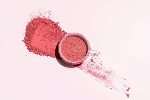A pink blush powder elegantly spread out on a light backdrop, with an open container This image