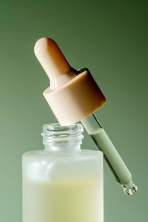 An isolated close-up of a serum dropper bottle with a droplet on a green background, perfect for