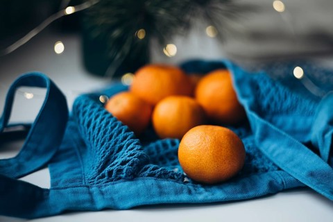 Fresh tangerines placed inside a vibrant blue string bag, set against a softly lit holiday