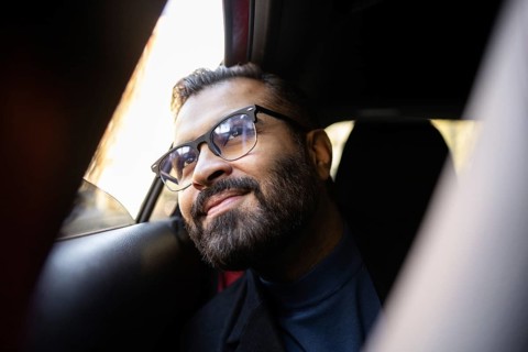 Indian businessman rides in a car on a sunny winter day, smiling warmly and looking slightly