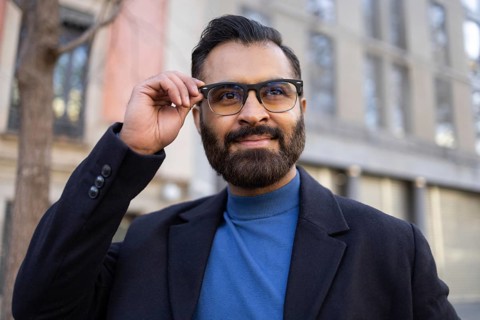 An Indian businessman in stylish winter attire, adjusting his glasses while smiling confidently
