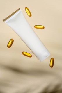 Top view of a blank white cosmetic tube floats amidst golden oil capsules, all set against a soft