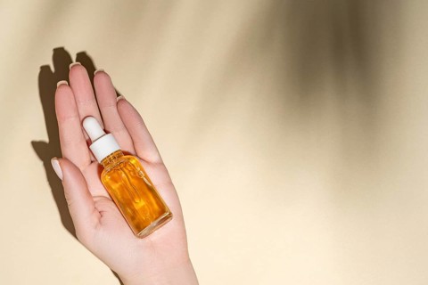 Top view of a cropped unrecognizable female hand holding a transparent dropper bottle filled with a