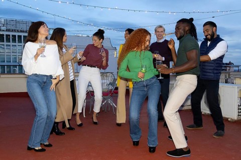 A lively group of friends celebrating on a rooftop, enjoying music and drinks They dance and laugh