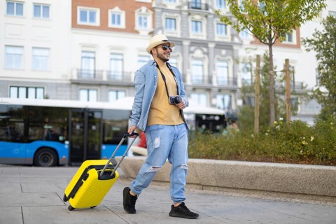 A stylish Latino transgender man strolls through the city with a camera and a vibrant yellow