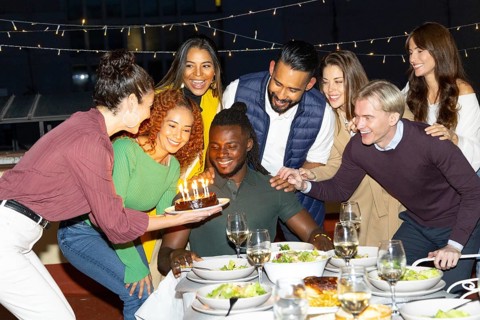 A joyful group of friends gathered at a vibrant outdoor birthday party, enjoying food and wine