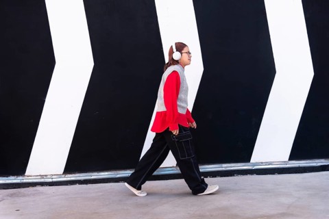 Latina woman in a vibrant red shirt and headphones walks confidently against a bold black and white
