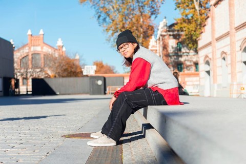 A young Latina woman in a red shirt and black pants sits on a concrete bench in an urban area It's