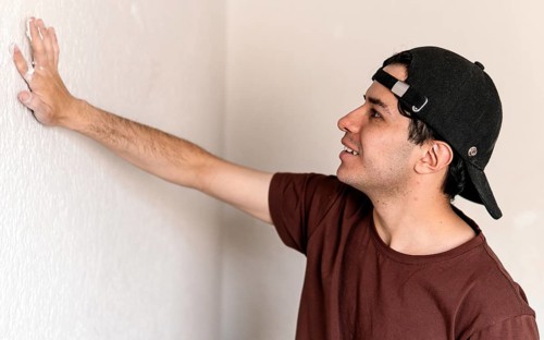 A young man inspects a wall closely during a home remodeling project, poised to begin his next task