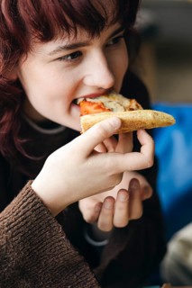 A young woman with red hair joyfully eats a slice of pizza, focusing on the flavor and her dining