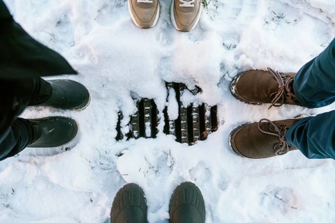 Four pairs of shoes and boots encircle a snow-covered drain in Stockholm, capturing a cozy glimpse
