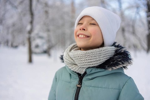 A young girl stands amidst a snowy landscape, wearing a warm scarf and hat, radiating happiness.