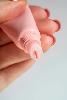 Cropped unrecognizable woman's hand applying a shiny lip balm from a pink tube, showcasing cosmetic